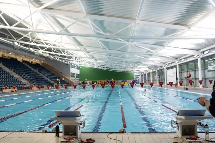 A fifty-metre competition pool with empty lanes, starting blocks in the foreground and tiered spectator seating along one side.